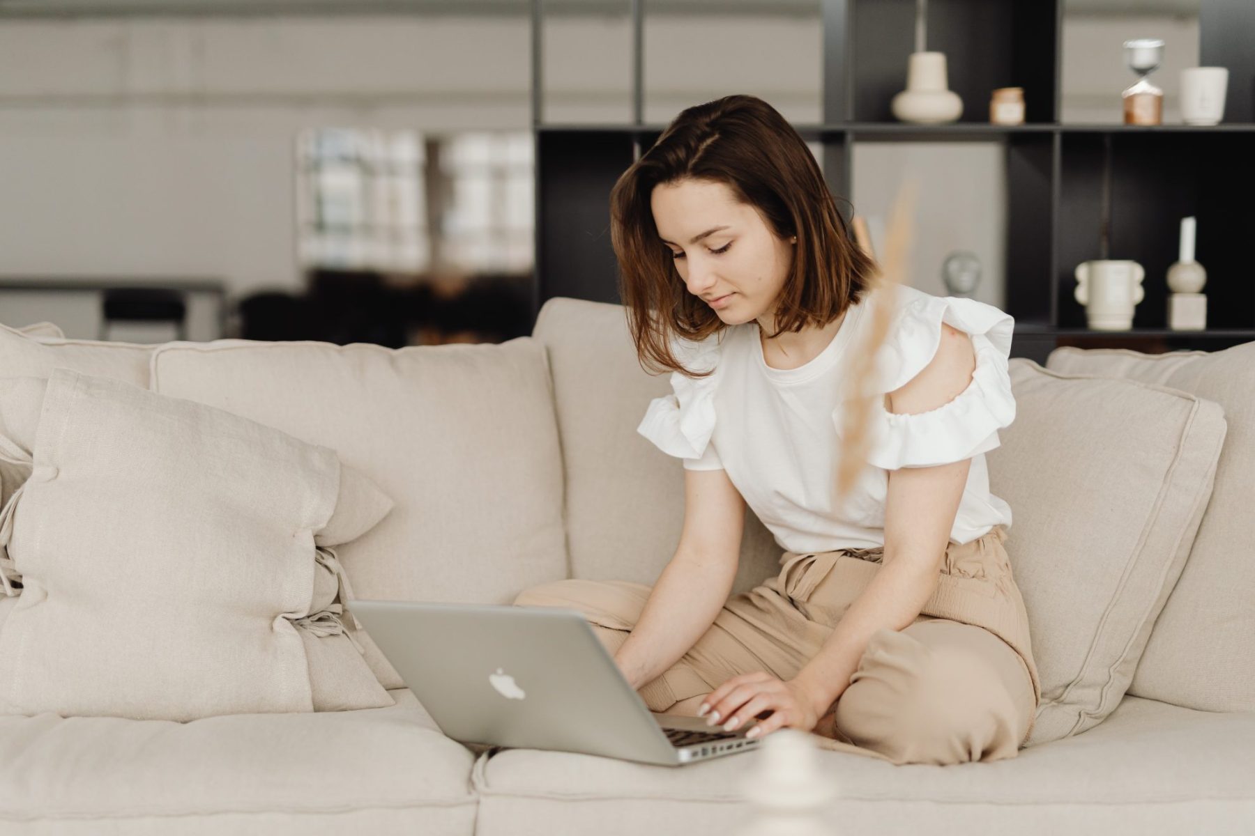 Woman in a white top and tan pants using work from home tools on her computer.